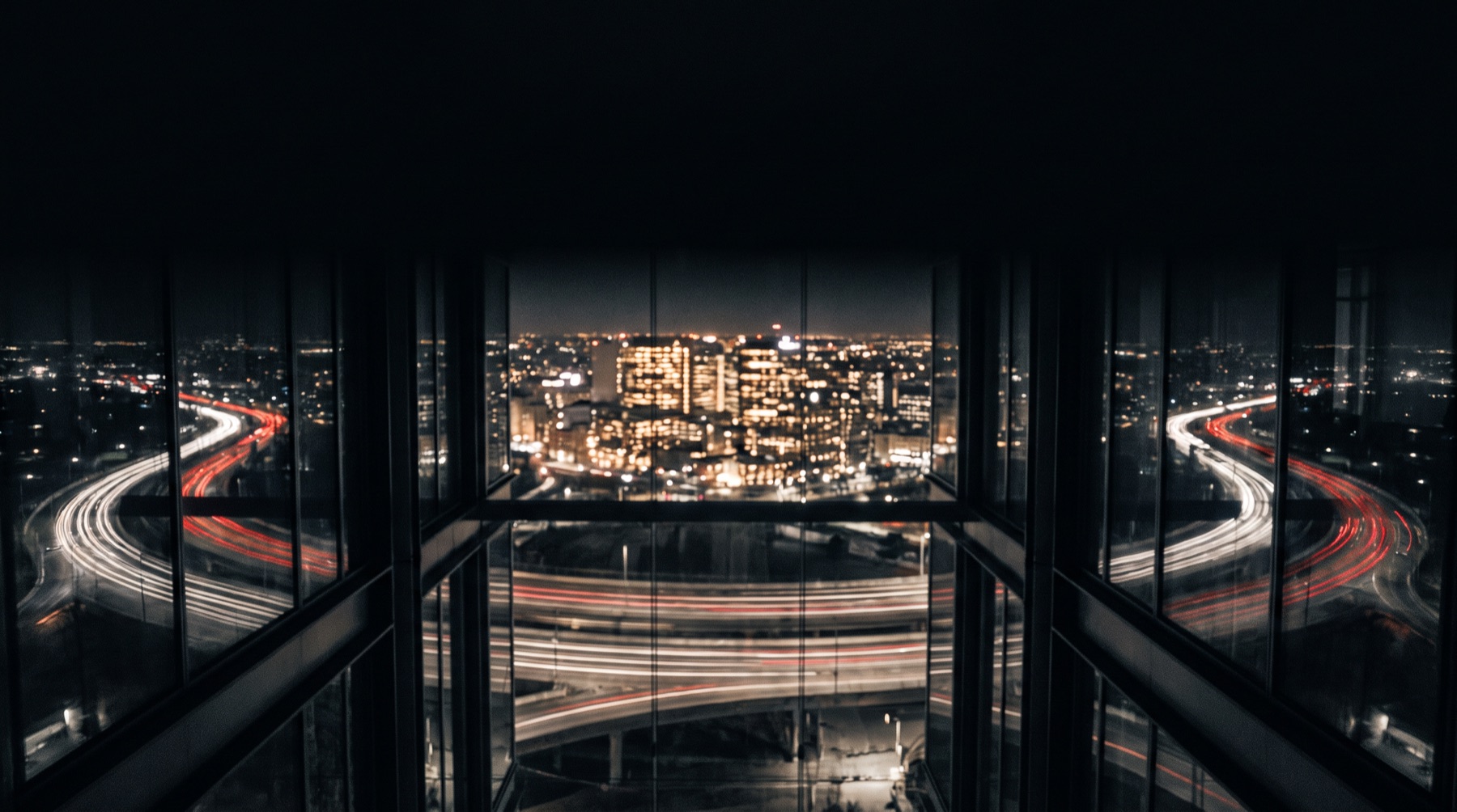 A night city from above, traffic light trails curving in arcs around one bright district.