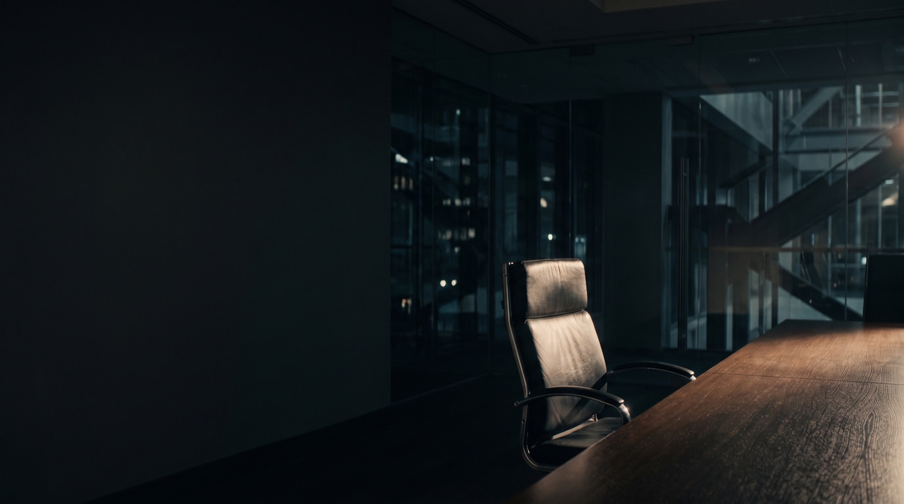An empty executive chair at a dark boardroom table, one hard light across the surface.